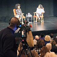 Esi Edugyan and Amanda Parris on stage with the audience and cameraman in the foreground.