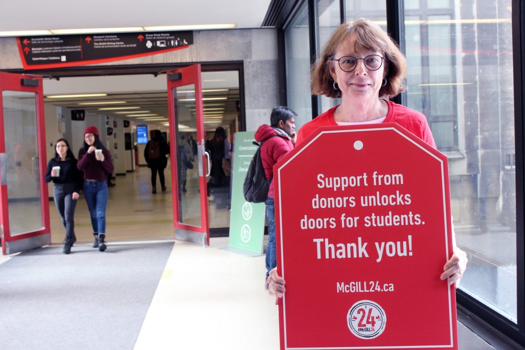 Dean Colleen Cook on Redpath Bridge holding up a poster that says "Support from donors unlocks doors for students"