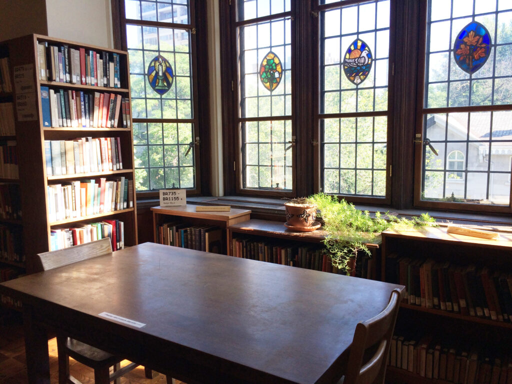 Corner of Birks Reading Room showing a wooden table, chairs, stained glass windows, and bookshelves.