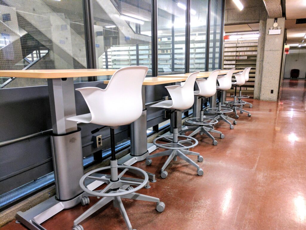 Row of high standing desks with white chairs.