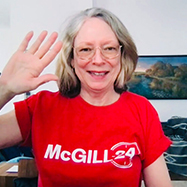 Colleen Cook in a red t-shirt at her desk waving to the camera