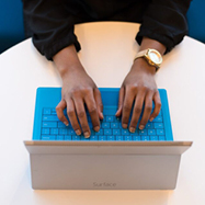 Hands seen from above on a blue Surface keyboard on a round table.