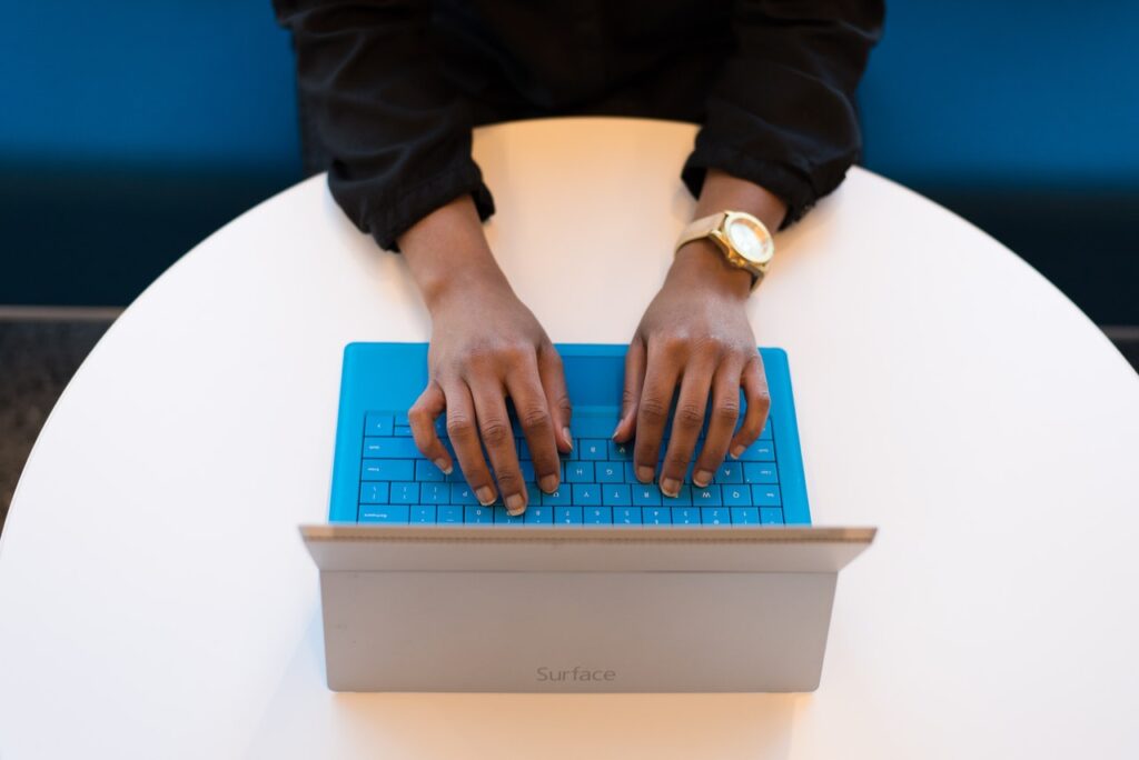 Hands on a blue Surface keyboard on a round table, seen from above.