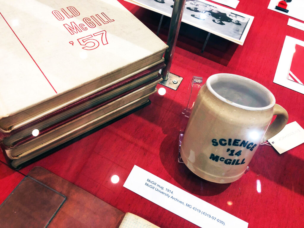 Objects in a display case, including a Science McGill '14 mug and 1957 McGill Yearbook.
