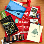 Red McGill Library tote bag laying flat with a book, bookmarks, cards, and candy on top of it.