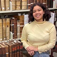 Lara Landauro smiling at the camera in front of a bookshelf filled with rare books.