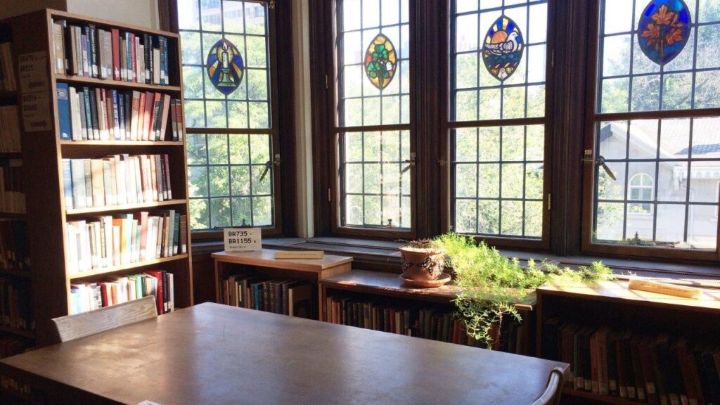 Wood table in the Birks Reading Room with stained glass windows, plants and books.