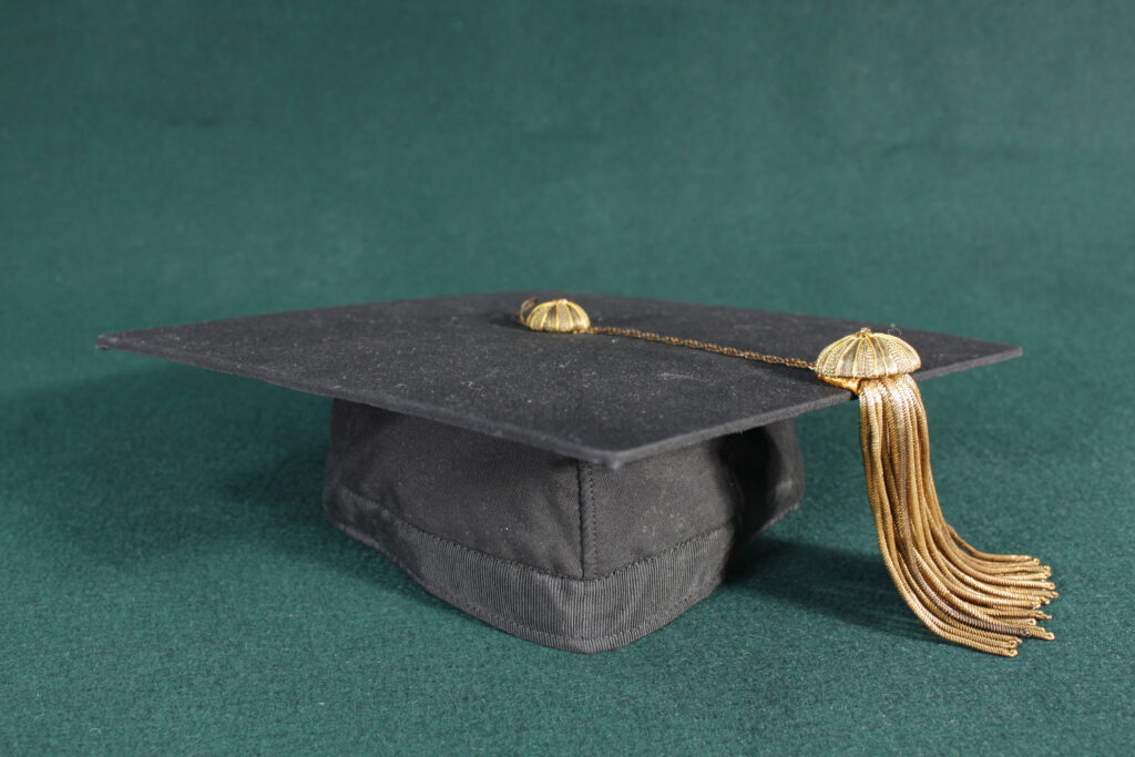 Archival graduation cap with gold tassel on a green felt surface.
