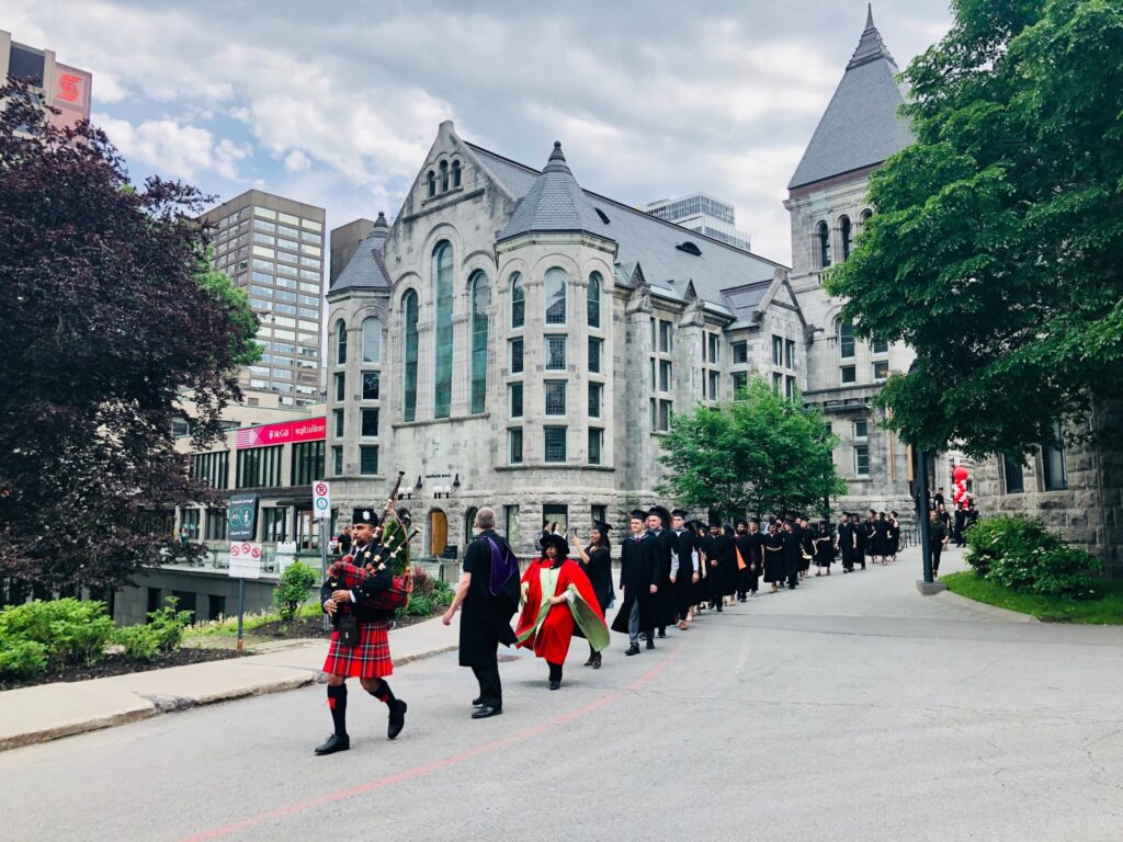 Graduate procession featuring bagpiper at the front and Redpath Hall and Redpath Library Building in background.