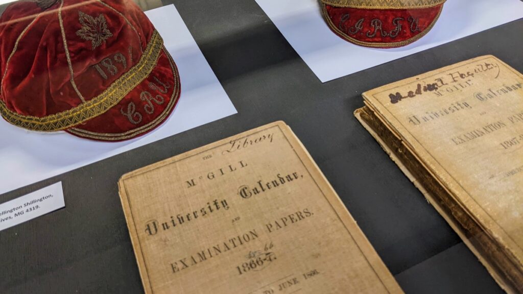 Installation view of the Convocation at McGill exhibition featuring two red felt caps and archival McGill examination papers.