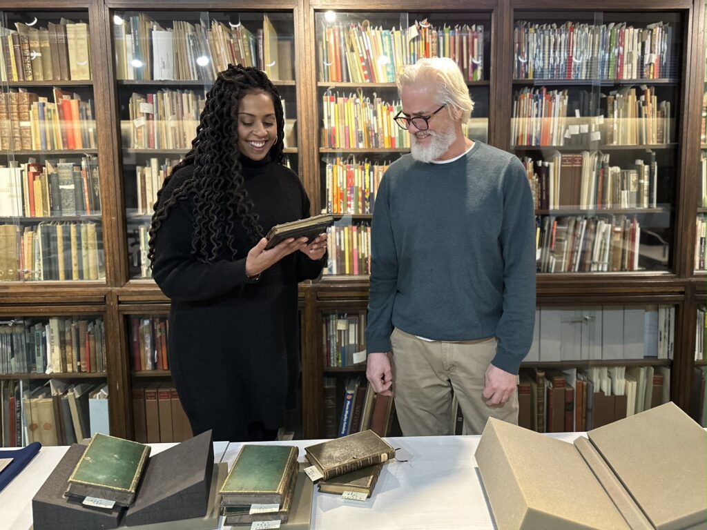 Paul Gross and Kimberley Rampersad looking at rare books with bookshelves behind them.