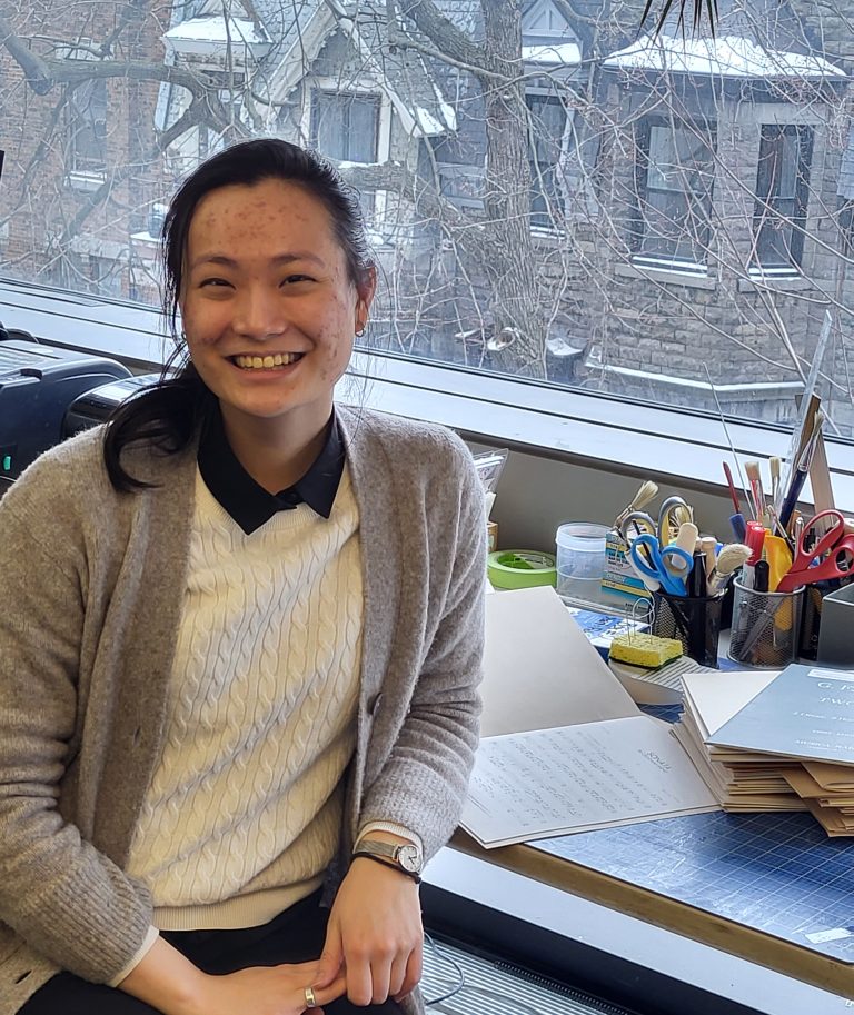 Ariel Pan smiling at the camera sitting at a desk in the Marvin Duchow Music Library.