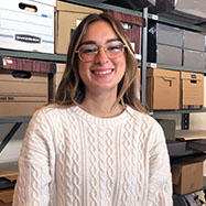 Emma Gallanti smiling at the camera standing in front of a shelving unit filled with boxes.