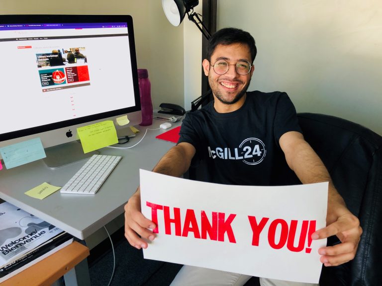 Mohammad Junaid Arif sitting at his desk, smiling at the camera, holding a sign that says Thank You! in red.