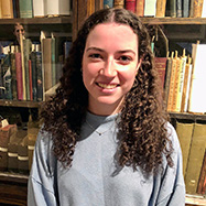 Olivia Dalton smiling at the camera standing in front of bookshelves.
