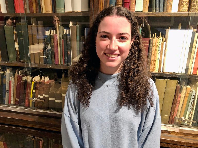 Olivia Dalton smiling at the camera standing in front of bookshelves.