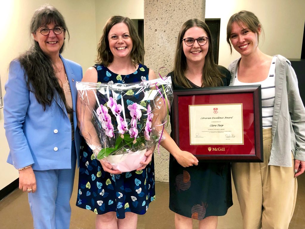 Dean Guylaine Beaudry, Dawn McKinnon, Clara Turp, and Ana Rogers-Butterworth smiling at the camera holding the framed award and orchid.