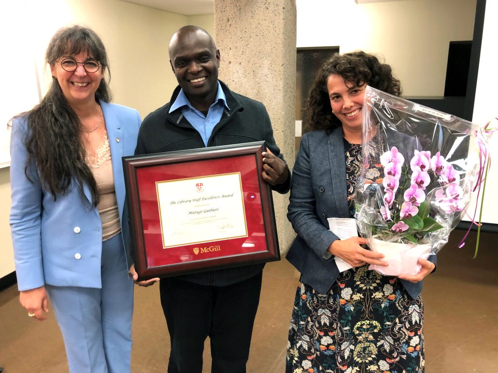 Dean Guylaine Beaudry, Mutugi Gathuri, and Alexandra Kohn smiling at the camera holding the framed award and orchid.
