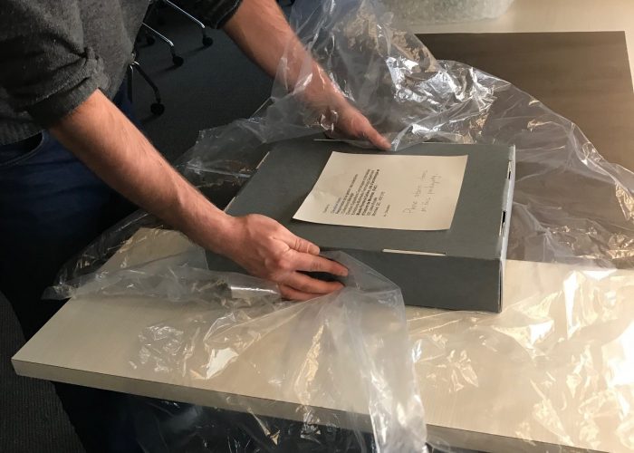Art packer places final packaging touches on box to be transported.