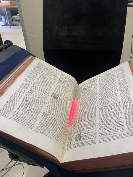 Process of digitizing a large folio using the Cobra overhead scanner at the Digitization Lab showing book open and red light in middle.